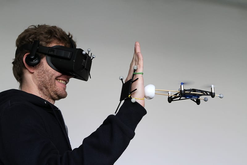 Person mit VR-Headset und Motion-Capture-Markern interagiert mit einer Drohne